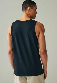 Sort ærmeløs tanktop med rund halsudskæring, glat tekstur og lige kant, båret af en person set fra ryggen.
