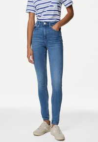 Vaqueros de cintura alta en un diseño ajustado con un lavado más claro, denim texturizado y bolsillos frontales, combinados con una camiseta de rayas y zapatillas.