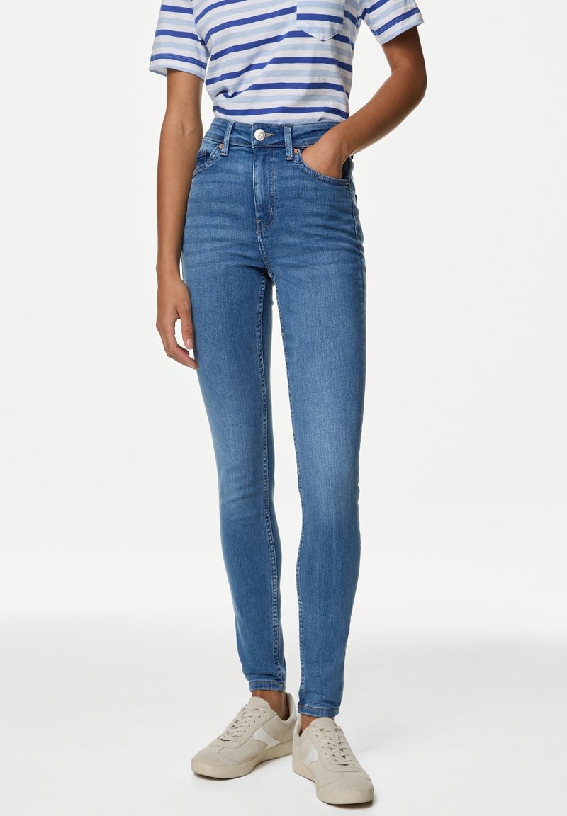 Vaqueros de cintura alta en un diseño ajustado con un lavado más claro, denim texturizado y bolsillos frontales, combinados con una camiseta de rayas y zapatillas.