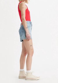 Röd ribbad linne kombinerat med ljusblå högmidjade denimshorts. Har en mjuk textur och klassisk femfickdesign, bärs med krämfärgade sneakers.