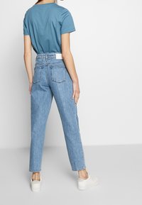 Vaqueros de denim azul claro con una cintura alta, pierna recta y dos bolsillos traseros; combinados con una blusa azul de manga corta y zapatillas blancas.