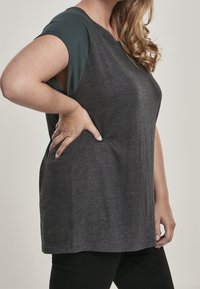 Camisa de manga corta gris con detalles en verde azulado oscuro, corte relajado y textura suave. Cuenta con bolsillos laterales y un cuello redondo.