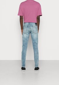 Vaqueros de denim de color azul claro con un corte ajustado, acabado desvaído y dos bolsillos traseros. Llevados con una camisa de manga corta rosa y zapatillas negras.