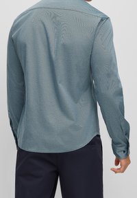 Langärmeliges Hemd aus strukturiertem blauem Stoff mit dezentem Fischgrätmuster, versehen mit einem abgerundeten Saum und knöpfbaren Manschetten.