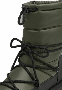 Zielony ocieplany but z wyściełaną cholewką, czarnymi sznurowadłami i teksturowaną gumową podeszwą. Regulowane zapięcie u góry dla lepszego dopasowania.