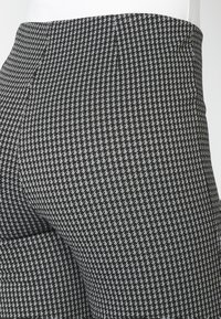 Leggingi z vzorcem črno-belega houndstooth, prilegajočega kroja. Narejeni iz raztegljivega materiala, z visokim pasom in brez žepov.