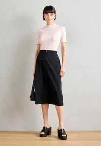 Rosa gerippter Kurzarm-Top mit hochgeschlossenem Design, kombiniert mit schwarzen weiten Culottes mit Taschen. Schwarze Plateausandalen runden den Look ab.