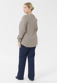 Blusa marrón a rayas con mangas largas, textura suave y dobladillo redondeado, combinada con unos vaqueros de pernera recta en azul oscuro y zapatos negros.