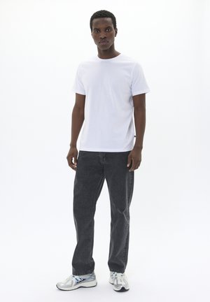Hvid crew neck t-shirt, kombineret med mørkegrå jeans. Modellen bærer sølv- og blå sportsko, præsenteret mod en ensfarvet hvid baggrund.