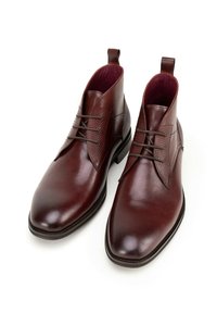 Hnědé kožené kotníkové boty s elegantním designem, texturovanými bočními panely a hladkým vrškem. Mají šněrování a poutka pro snadné obutí.