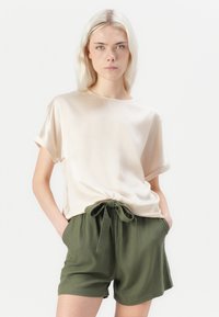 Lys beige satin topp med rullet korte ermer, kombinert med olivengrønne shorts med bundet belte. Enkel, avslappet design.