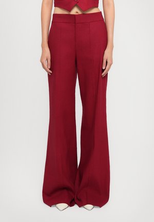 Red wide-leg trousers with a tailored fit, featuring a smooth texture and double front pleats, paired with white pointed-toe shoes.