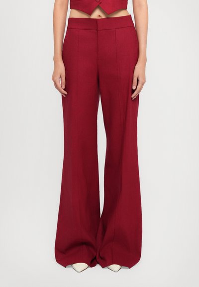 Pantalones rojos de pierna ancha con un corte entallado, que presentan una textura suave y doble pliegue frontal, combinados con zapatos blancos de punta afilada.