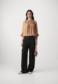 Satin blouse in soft peach, featuring a gathered neckline and puffed sleeves, paired with high-waisted black trousers and white shoes.