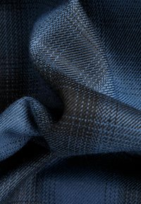 Gevloeide stof met een zwart en blauw geblokt patroon, met een zachte textuur en een lichte glans, die ingewikkelde details toont.