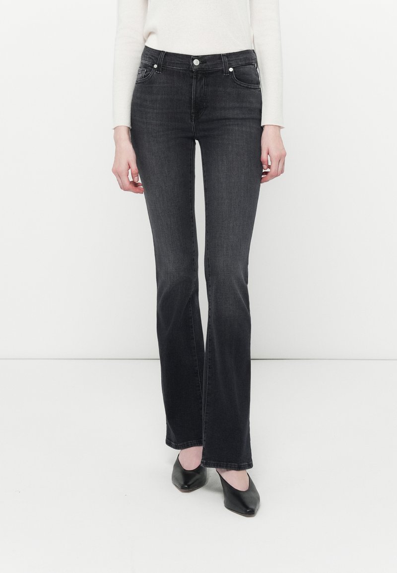 Jeans in denim nero a campana con bottone in vita, tasche frontali e una texture sbiadita. Indossati con tacchi neri a punta.