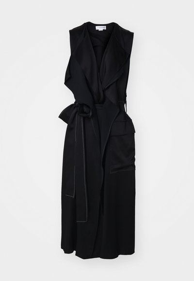 Black sleeveless wrap dress with a front drape, features a tie belt, angled pockets, and subtle white stitching along the edges.