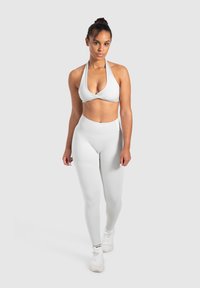 Weißer Sport-BH mit einem Halterneck-Design, kombiniert mit passenden hochtaillierten Leggings. Glatte Textur, figurbetonte Silhouette, minimalistischem Stil.
