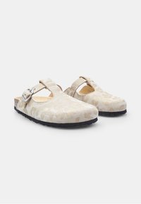 Beige suede clogs featuring a subtle abstract pattern, a strap with metallic hardware, and a textured black rubber sole.