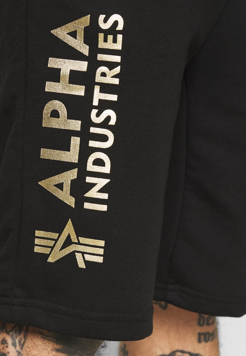 Herren Trainingsanzüge | Alpha Industries BASIC FOIL PRINT Jogginghose black/yellow gold/schwarz - GC74757 Herren Trainingsanzüge | Alpha Industries BASIC FOIL PRINT Jogginghose black/yellow gold/schwarz - GC74757