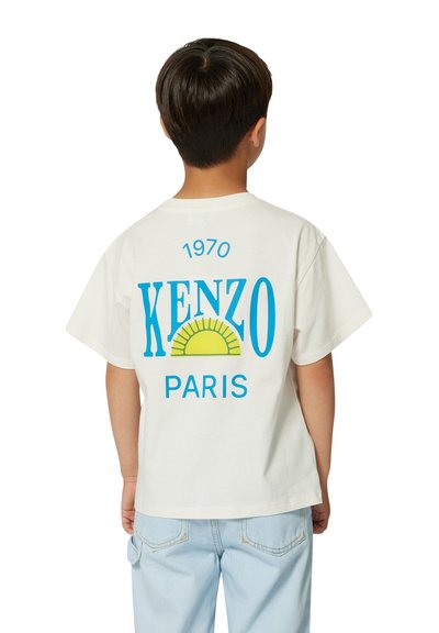 T-shirt en coton blanc avec un texte graphique bleu "KENZO" et "PARIS", comportant un design de soleil jaune. Manches courtes et coupe décontractée.
