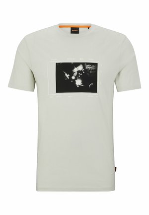 T-shirt gris clair à col rond avec un graphique en noir et blanc de mains produisant des étincelles de feu sur le devant et un col bordé d'orange.
