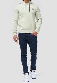 Sudadera verde claro con cordones, logo en el pecho; combinada con pantalones ajustados de navy oscuro y zapatillas blancas. Material suave, ajuste casual.