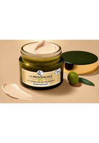 Pot en verre vert avec un couvercle doré, contenant une crème légère. L'étiquette présente le texte "LA PROVENÇALE BIO," et un échantillon de crème est sur la surface.