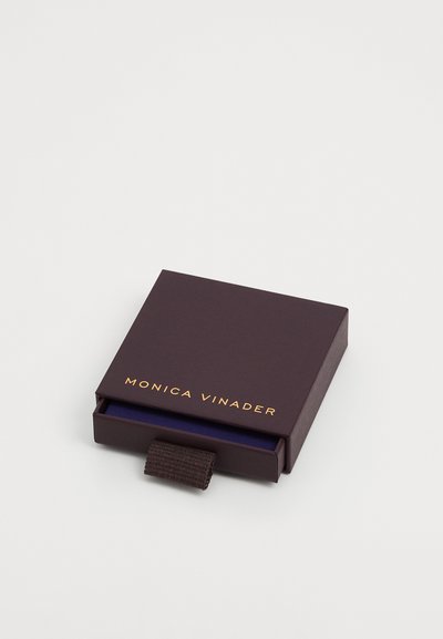 Cutie de bijuterii maro cu text auriu "MONICA VINADER", având o bandă de tragere și un interior închis. Formă pătrată, textură netedă, design minimalist.
