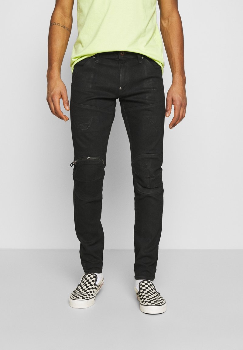 Černé džíny z denimu s zipy na kolenou, opotřebenými detaily a slim fit, doplněné kostkovanými slip-on botami.