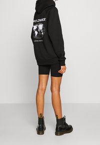 Black hoodie with white graphic featuring a globe and text on the back, paired with black shorts and black lace-up ankle boots.