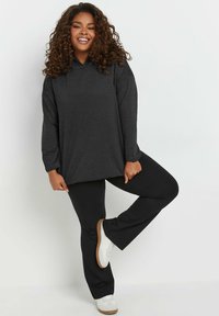 Sudadera negra con un corte relajado y mangas largas, combinada con pantalones negros y zapatillas deportivas blancas, mostrando un estilo casual.