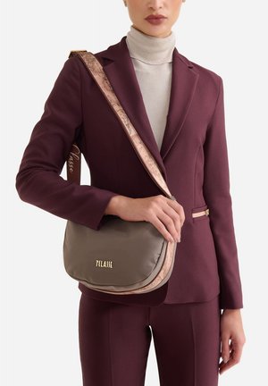 Borsa a tracolla grigia in nylon con tracolla rosa con motivo e logo dorato, caratterizzata da una forma arrotondata e una texture morbida, tenuta da una persona.