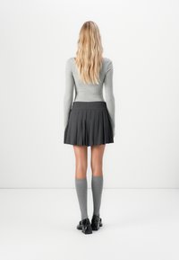 Grå strikket langermet topp, svart plisserte skjørt, grå sokker til knærne og svarte sko. Fokuser på tekstur og lagdelt design.