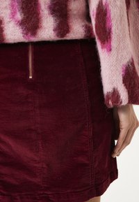 Roze fuzzy trui met abstracte donkere patronen, gecombineerd met een bordeaux corduroy rok met een zijrits en verticale ribbels.