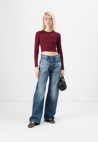 Burgunderfarget langermet crop topp, høy midje falmede blå flared jeans, svart teksturert håndveske og leopardmønstret slip-on sko.
