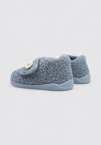 Chaussures à enfiler en textile bleu avec une texture douce et bouclée, semelles en caoutchouc, et un patch décoratif en forme de fleur sur le dessus. Nom de la marque "igor" visible.