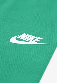 Tissu vert avec une texture nervurée arborant un logo Nike blanc, stylisé dans unePolice en gras, positionné de manière proéminente.