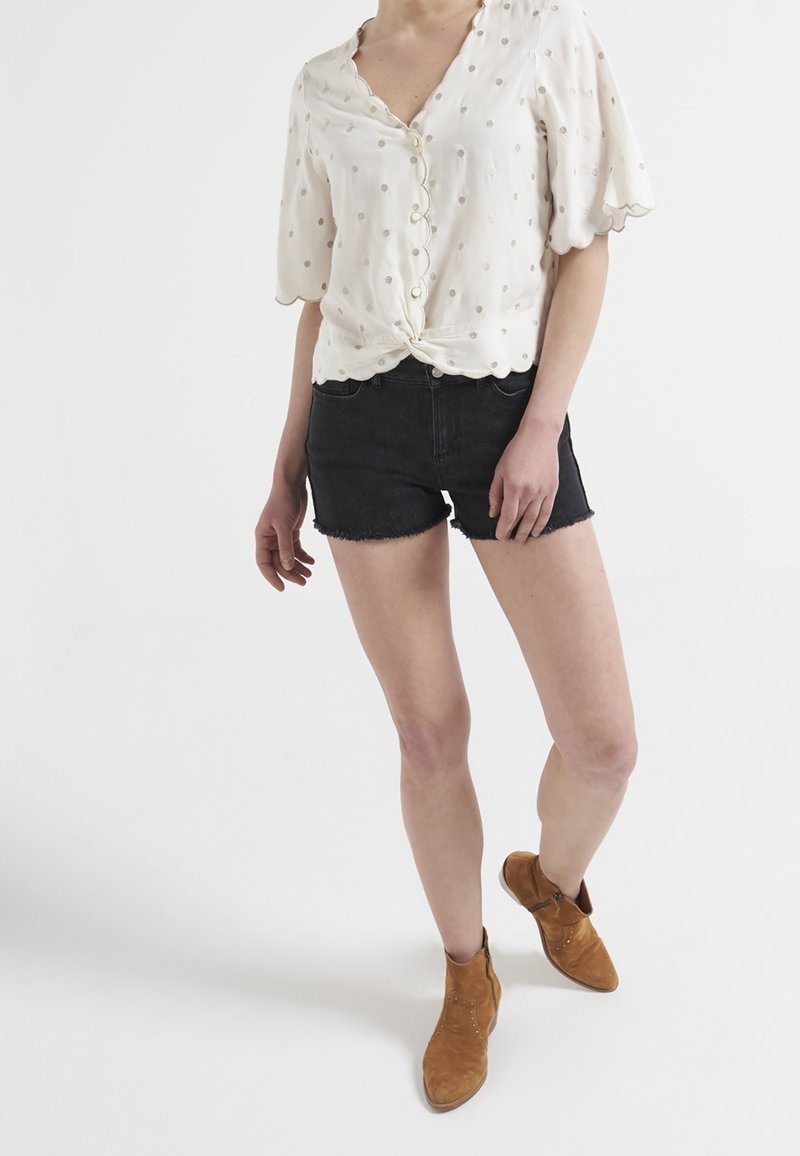 White button-up blouse with short flutter sleeves, floral embroidery, knotted front detail, paired with black denim shorts and tan ankle boots.