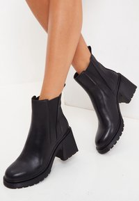 Czarne botki za kostkę o gładkim skórzanym wykończeniu, z elastycznymi panelami bocznymi i masywnymi, teksturowanymi obcasami. Elegancki, zaokrąglony kształt nosa.