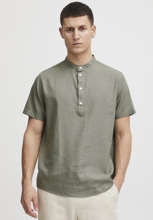 Camisa de manga corta de color verde oliva con cuello mao, con cierre de botones en la parte delantera y un corte relajado en una tela texturizada.