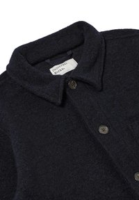 Giacca camicia in lana di un blu navy scuro, con colletto, bottoni frontali e una tasca sul petto. Tessuto morbido con una finitura sottile.