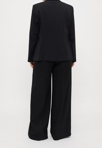 Czarna dopasowana marynarka z klapami z wycięciem, zestawiona z szerokimi spodniami. Gładka tkanina o matowym wykończeniu i minimalistyczne detale.