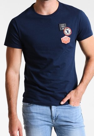 Marineblaue kurzärmlige T-Shirt aus Baumwolle, mit vier verschiedenen Aufnähern auf der Vorderseite, Rundhalsausschnitt und figurbetontem Schnitt.