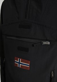 Schwarze Jacke mit hohem Kragen, Reißverschlusstasche, Klettakzenten und einem roten Aufnäher mit der norwegischen Flagge. Strukturierte Stoffoberfläche.