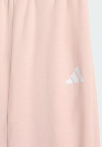 Světle růžové tepláky s jemnou texturou, elastickým pasem a bílým logem Adidas na straně. Jednoduchý, elegantní design.