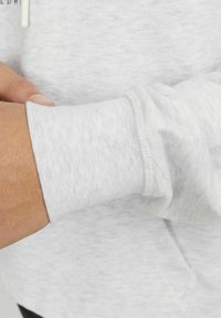 Lichtgrijze sweatshirt met een geribbelde manchette en zachte textuur. Close-up van het polsgebied toont een naadloze afwerking en een dunne, relaxte pasvorm.