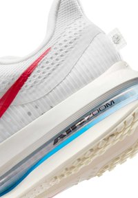 Baskets blanches avec un accent rouge, tige en mesh, et une unité Air Zoom visible dans une semelle bleue translucide avec un motif de grip texturé.