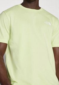 Světlě žluté tričko s krátkým rukávem vyrobené z měkké látky, s bílým logem na levé části hrudi. Kulatý výstřih a volný střih.