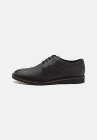Chaussure formelle en cuir noir pour homme avec lacets, talon bas et bordure subtile marron sur la semelle, vue de côté gauche sur fond blanc.